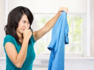 woman pinching her nose and holding a smelly shirt in her hand.